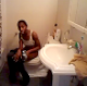 A black girl is video-recorded sitting on a toilet taking a crap. She yells at the videographer for recording her. There are no audible pooping sounds.